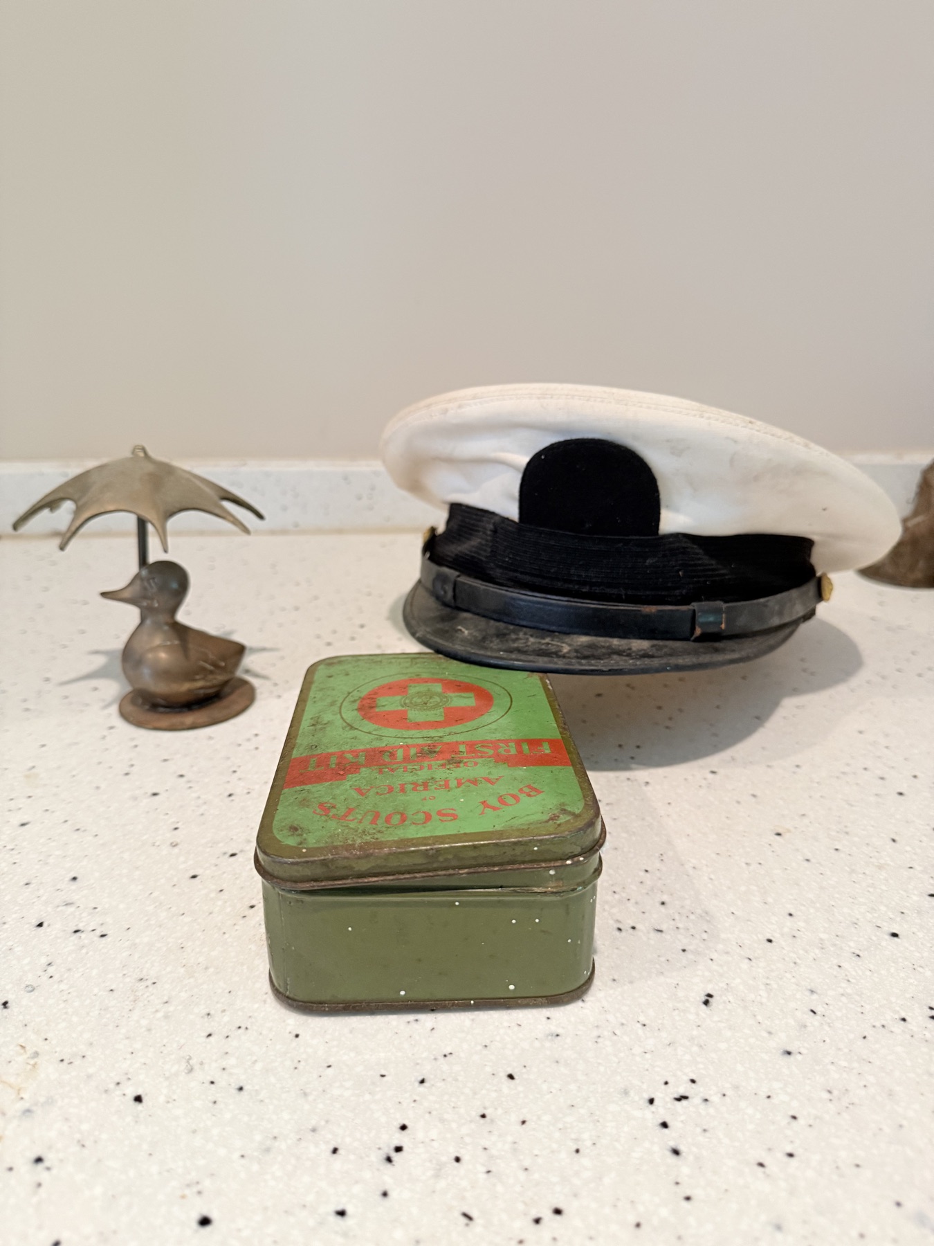 Green vintage first-aid tin displayed with white sailor caps and a small metal bird figure