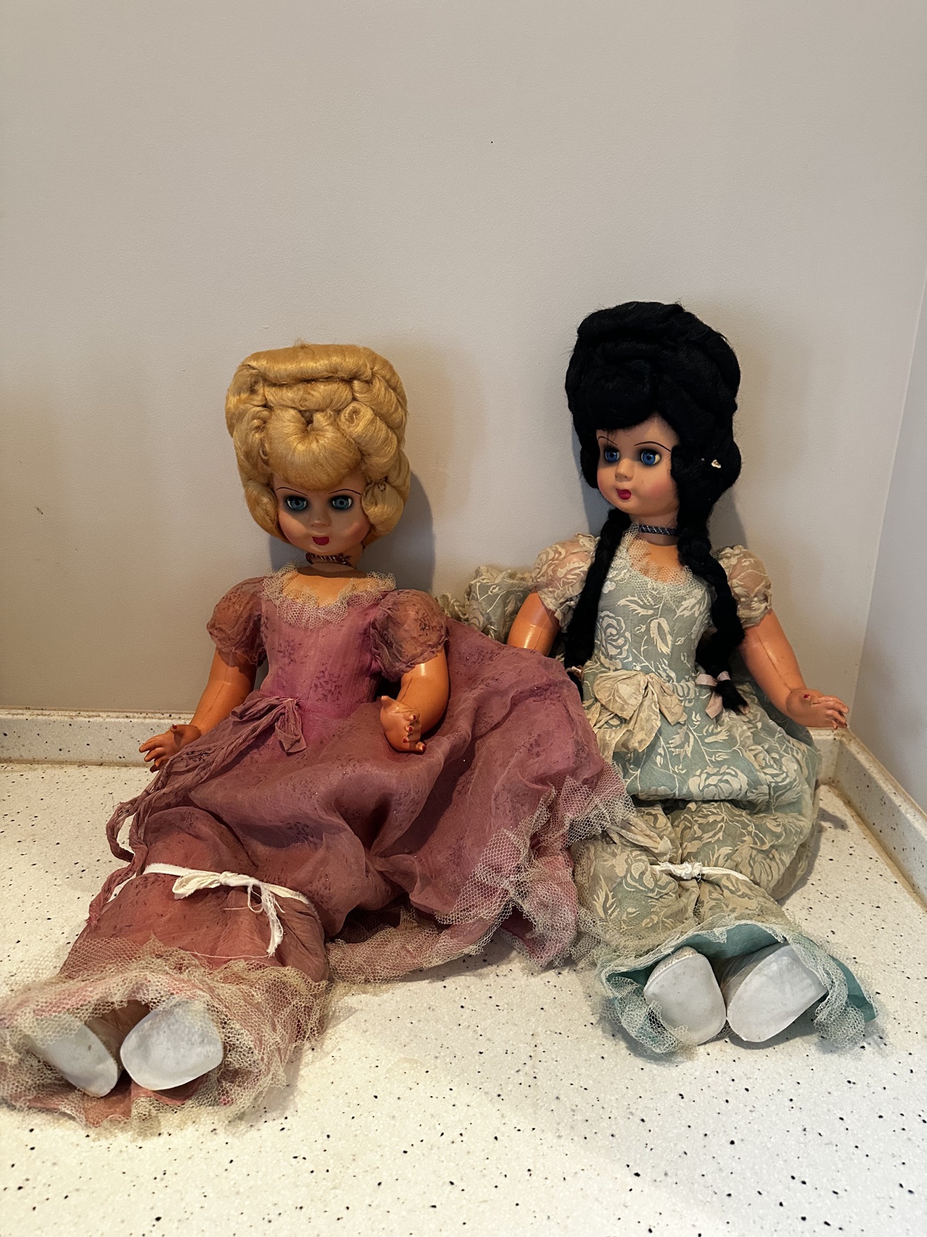 Two vintage fashion dolls seated together in pink and blue dresses